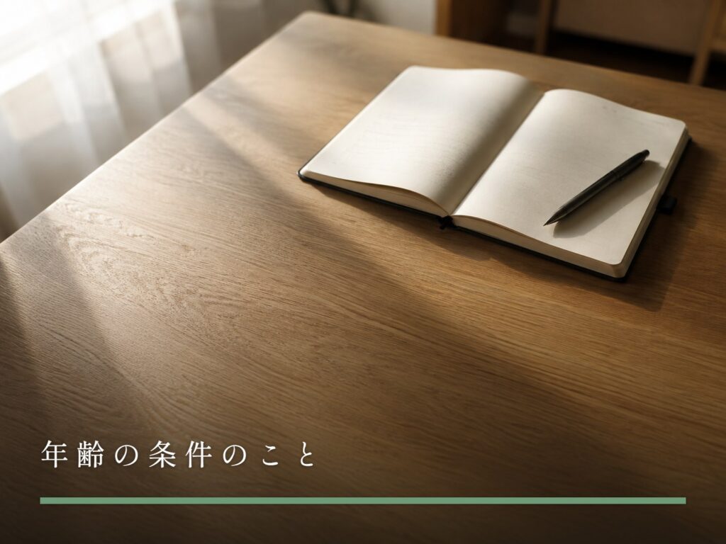 木のテーブルに置かれた、開かれたままの手帳とボールペン（年齢の条件のこと）