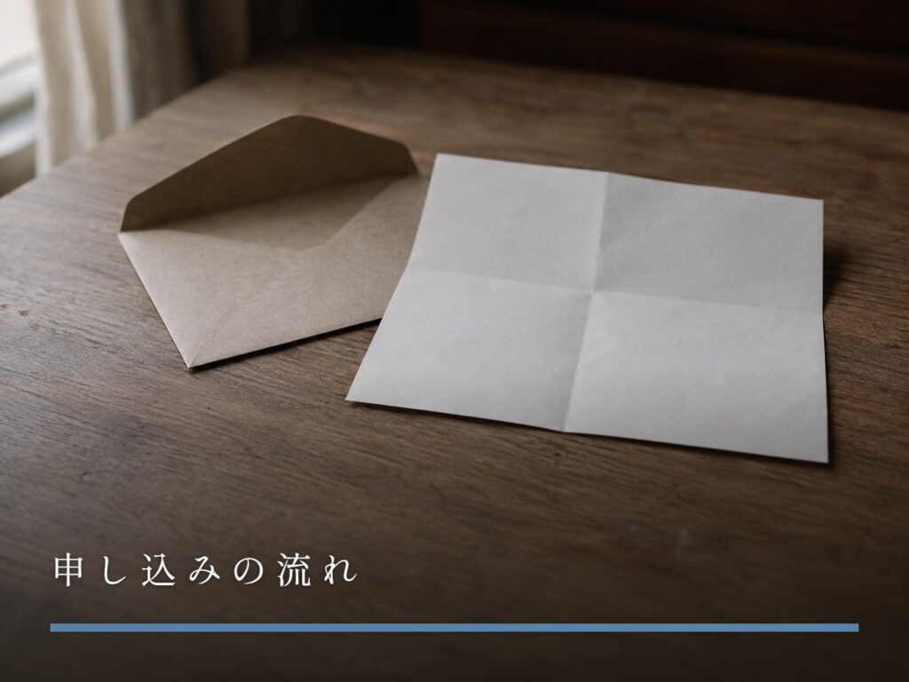 木の机に置かれた、封を開けた封筒と折り目のついた一枚の紙（申し込みの流れ）
