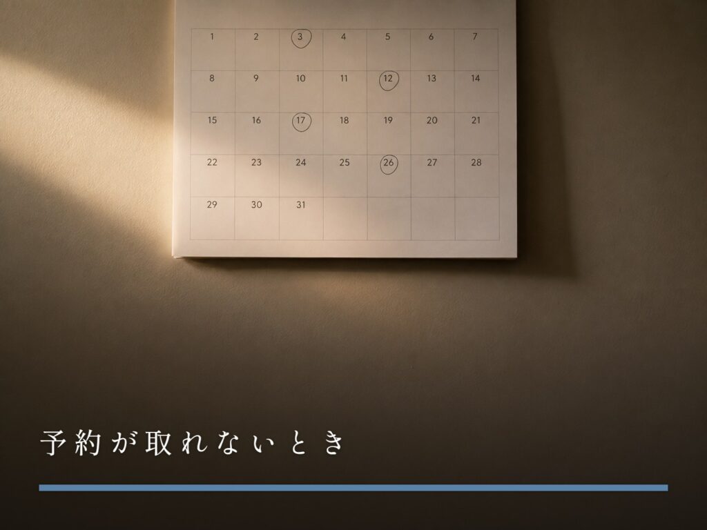 壁に掛かった紙の月間カレンダー。いくつかの日付に手書きの丸印（予約が取れないとき）