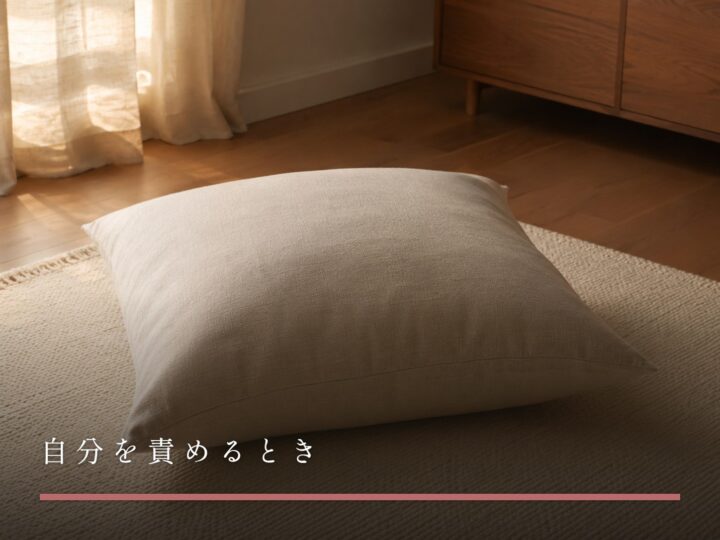 照明を落とした部屋の床のラグに置かれた大きなクッションひとつ（自分を責めるとき）