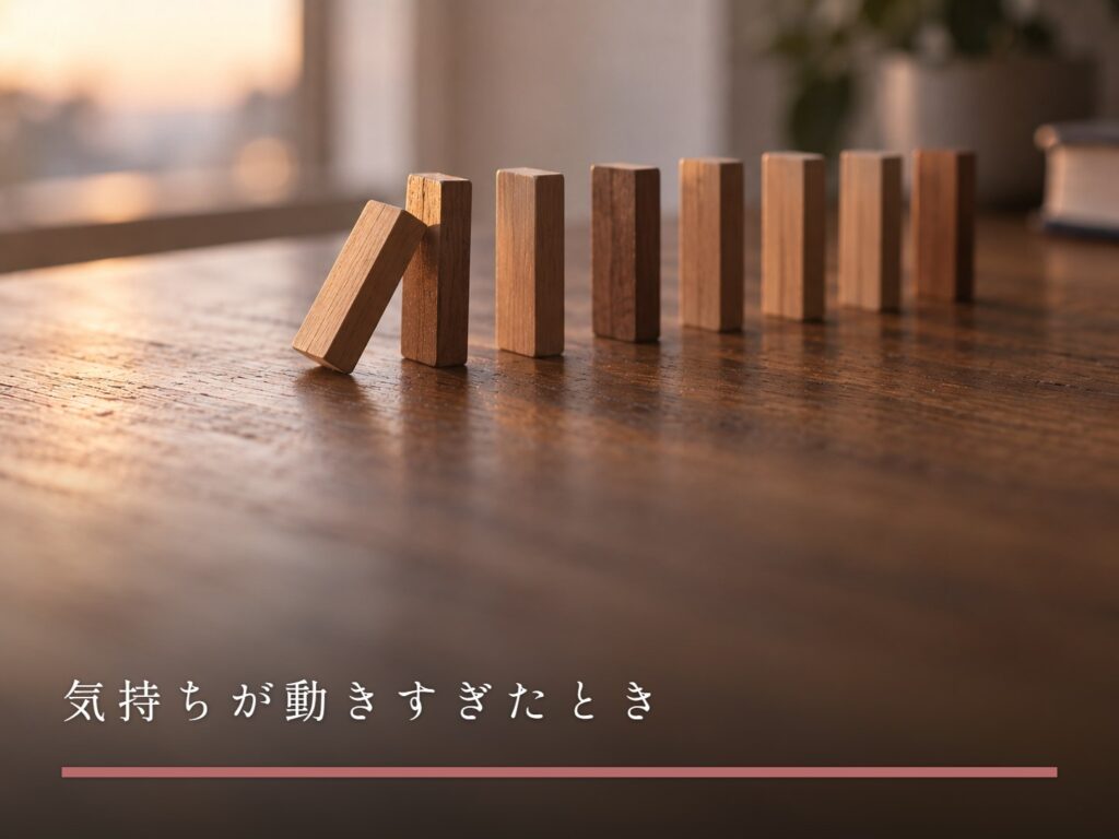 木の机に並べられたドミノの列。先頭の一枚が倒れかけて止まっている（気持ちが動きすぎたとき）